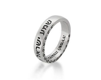 May include: A silver ring with Hebrew text engraved around the band. The ring has a smooth, polished finish and a simple, elegant design. The text is in a dark color, contrasting with the silver. The ring is a piece of jewelry.