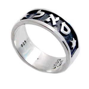 Puede incluir: Un anillo de plata de ley con letras hebreas y recortes de estrellas. El anillo tiene una banda oscura y texturizada con letras blancas en relieve. El interior del anillo está estampado con "925" y otras marcas. Una joya elegante.