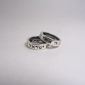 May include: Two silver rings with Hebrew text inscribed on them. The rings are stacked on top of each other.