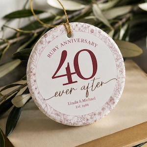 May include: A round white ceramic ornament featuring a delicate floral border and the maroon text Ruby Anniversary 40 ever after, personalised with the names Linda & Michael and the date Est. 1986, suspended by a thin gold string.