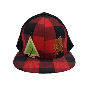 May include: A black and red plaid baseball cap with a brown felt patch of a Bigfoot silhouette and a green and white tag that says "LIDS" on the front.