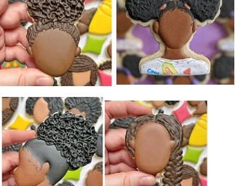 May include: Four cookie cutters in the shape of a person's head with different hairstyles. The hairstyles include two buns, a side braid, and a curly afro. The cookie cutters are made of a light brown material and are designed to be used for baking.