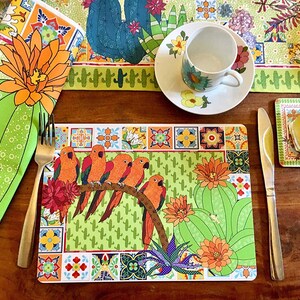 Puede incluir: Una mesa vibrante con un mantel individual con loros naranjas posados en una rama, dise&ntilde;os de cactus y flores. Incluye una servilleta, un camino de mesa, una taza de t&eacute;, un platillo y un posavasos a juego. La paleta de colores incluye verde, naranja y blanco.