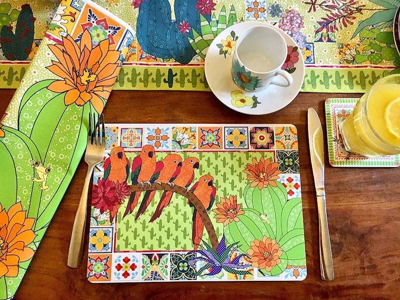 Puede incluir: Una mesa vibrante con un mantel individual con loros naranjas posados en una rama, dise&ntilde;os de cactus y flores. Incluye una servilleta, un camino de mesa, una taza de t&eacute;, un platillo y un posavasos a juego. La paleta de colores incluye verde, naranja y blanco.