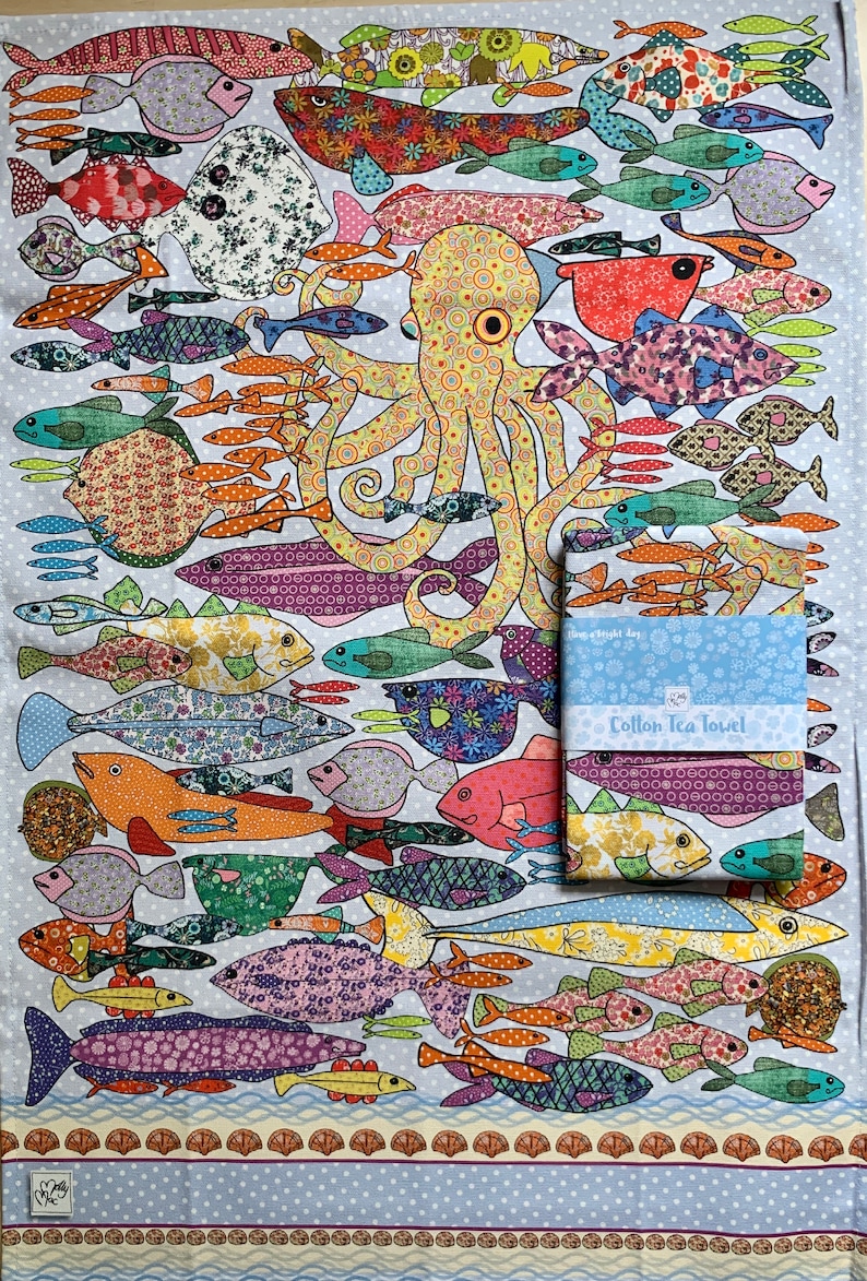 May include: A colorful cotton tea towel with a whimsical design of an octopus surrounded by various fish. The towel features a blue background with white polka dots and a border of brown and yellow shells. The text "Cotton Tea Towel" is printed on the towel.
