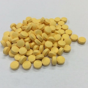 May include: A large pile of yellow round pills on a white surface.