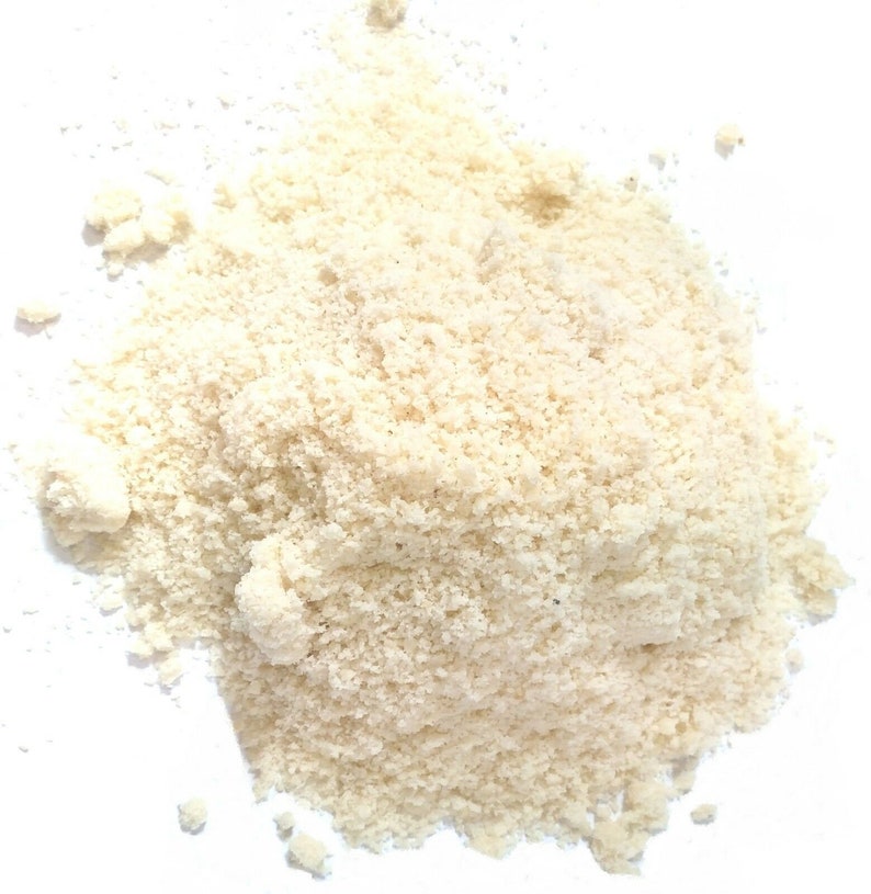 May include: A close-up of a pile of finely ground almond flour, a pale ivory colour, against a white background.