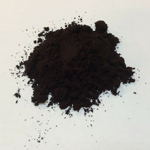 May include: A close-up of a pile of dark brown coffee grounds on a white surface.