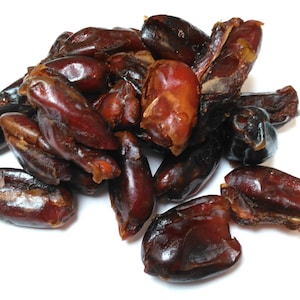 Puede incluir: Un montón de dátiles secos, algunos con la piel quitada, sobre un fondo blanco.