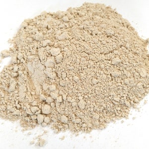 May include: A mound of light beige powder with a rough, granular texture. The powder looks finely ground, with small, uneven particles. The colour is a soft beige, and the overall appearance is dry and powdery.