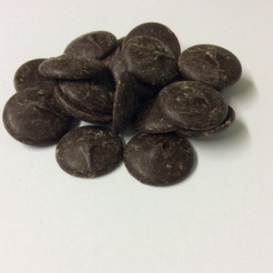 Op de afbeelding: Een stapel donkere chocolade bakschijven, ook wel chocolade chips genoemd, op een wit oppervlak.