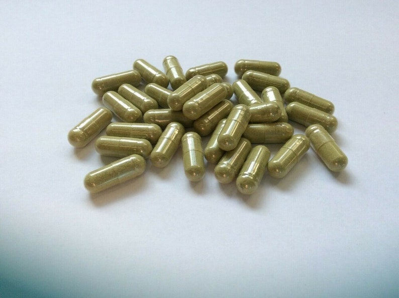 May include: A pile of green and brown capsules on a white surface.