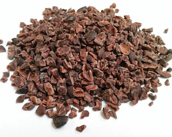 Puede incluir: Un montón de nibs de cacao marrón oscuro, con formas y texturas irregulares, sobre un fondo blanco. Los nibs son de un color marrón rico y terroso, lo que sugiere un sabor tostado. Ideal para mostrar ingredientes para hornear o hacer chocolate.