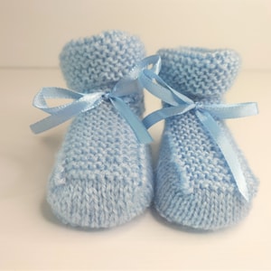 May include: A pair of light blue knitted baby booties with satin ribbon ties.