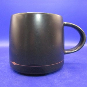 May include: A black ceramic mug with a thin, light brown line around the top edge. The mug has a rounded shape and a handle.