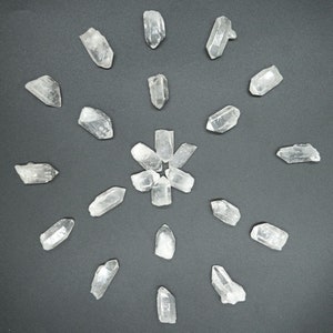 May include: A collection of clear quartz crystals arranged in a circular pattern on a dark grey background.