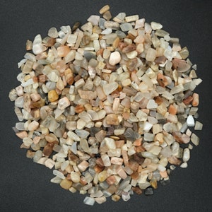 May include: A large pile of small, irregularly shaped, light brown, white and peach coloured moonstone chips.