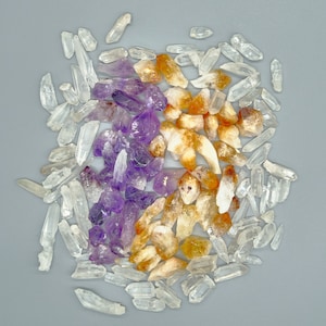 May include: A collection of amethyst, citrine, and clear quartz crystals. The crystals are arranged in a cluster on a grey background.