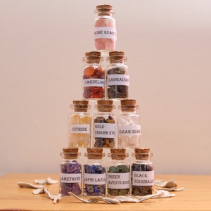 May include: A display of small glass bottles with cork stoppers, each containing a different gemstone and labelled with its name. Gemstones include Rose Quartz, Carnelian, Citrine, Gold Tigers Eye, Clear Quartz, Amethyst, Lapis Lazuli, Green Aventurine, and Black Tourmaline.