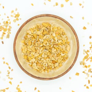 May include: A wooden bowl filled with small, yellow and white, irregularly shaped, polished stones. The bowl is on a white background, and there are some stones scattered around the bowl.