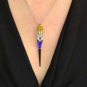 May include: A silver chain necklace with a pendant made of woven metal wire in purple, white, and yellow colors. The pendant is shaped like a teardrop with a pointed tip.