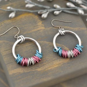 May include: A pair of silver hoop earrings with a ring of blue, pink, and silver metal rings around the hoop.
