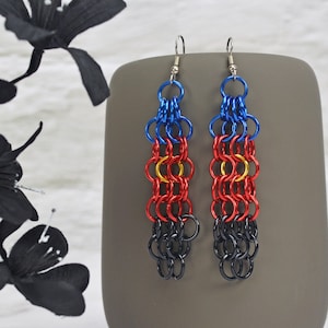 May include: A pair of long, dangling earrings with a chainmail design. The earrings are made of metal and are colored blue, red, yellow, and black.