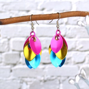 May include: A pair of dangle earrings with three layered teardrop-shaped charms. The charms are pink, gold, and blue.