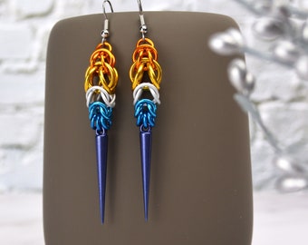 May include: A pair of long, dangling earrings with a blue, white, and orange color gradient. The earrings are made of metal and have a pointed tip.