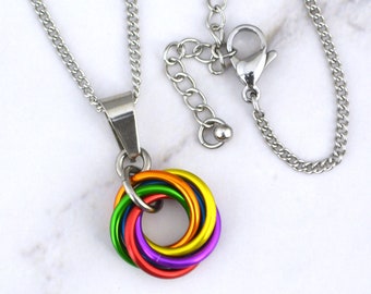 May include: A rainbow colored metal chain necklace with a silver chain and clasp. The pendant is a woven circle of rainbow colored metal.