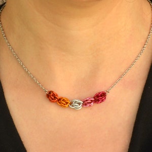 May include: A silver chain necklace with a row of five linked chainmail rings in orange, pink, white, pink, and orange.