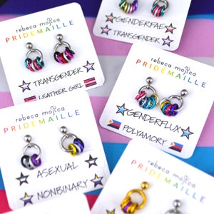 Several pairs of small mismatch pride earrings on cards. Earrings are chainmaille, with one link in each color of the flag. The flags depicted are genderflux, polyamory, asexual, nonbinary, transgender, leather girl, genderfae and intersex