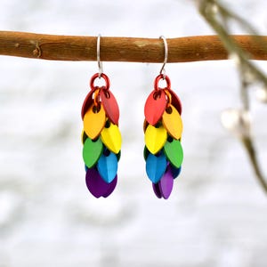 Puede incluir: Pendientes colgantes de colores arcoíris con un gancho plateado. Los pendientes están hechos de pequeñas escamas de metal en un patrón de arcoíris, comenzando con rojo en la parte superior y terminando con morado en la parte inferior.