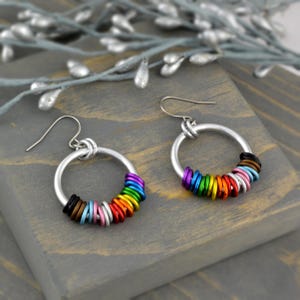 May include: Rainbow colored metal rings are strung around a silver hoop earring. The earrings have a silver hook closure.