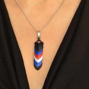 May include: A silver chain necklace with a pendant made of black, blue, red, and white interlocking scales. The pendant is shaped like a teardrop.