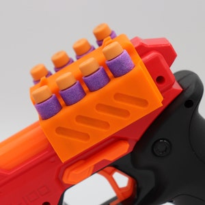 May include: A red and orange toy gun with a black handle and a clip full of purple and orange darts.