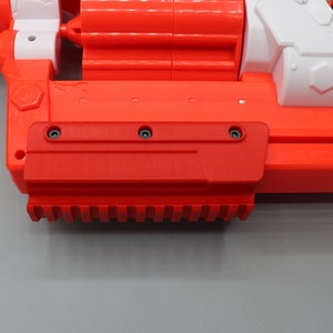 Op de afbeelding: Een rood en wit speelgoedpistool met een zwarte loop en een rode greep. Het pistool heeft een getextureerde greep en een zwarte trekker.