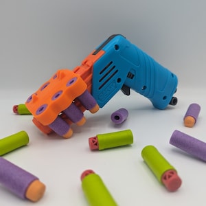 Op de afbeelding: Een blauw en oranje speelgoedpistool met een paars en oranje magazijn. Het pistool is geladen met paarse en groene foam darts.