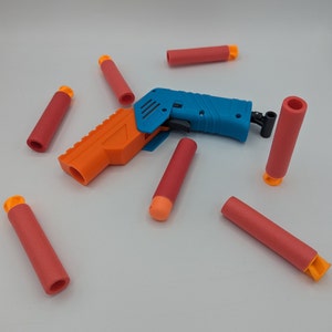May include: A blue and orange toy gun with a blue barrel and orange handle. The gun is surrounded by orange and red darts.