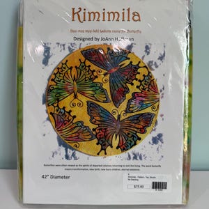 May include: A Kimimila pattern kit in plastic packaging featuring a circular design with colorful butterflies on a yellow background. The text reads Kimimila, Lakota name for Butterfly, Designed by JoAnn Hoffman, and 42" Diameter with details.