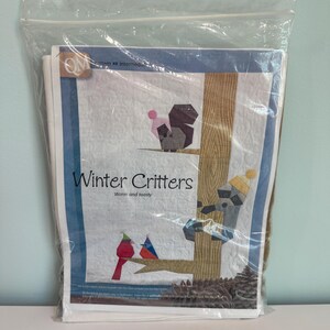 May include: A clear plastic bag containing a quilt pattern titled "Winter Critters." The pattern features a squirrel, cardinal, and raccoon on a tree branch. The text "Warm and toasty" is below the title.