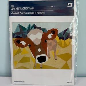 May include: A packaged quilt kit featuring a geometric cow design. The kit includes the text "the COW ABSTRACTIONS quilt" and "a Foundation Paper Piecing Project by Violet Craft". The cow illustration uses brown, white, and tan colors.