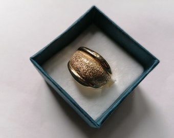 May include: A gold ring with a textured surface and a smooth, polished band. The ring is in a blue velvet box.