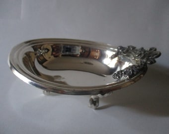 Könnte beinhalten: Eine ovale Servierplatte aus Silber mit verzierten Griffen und drei Füßen. Die Platte ist hochglanzpoliert und spiegelt die Umgebung wider.