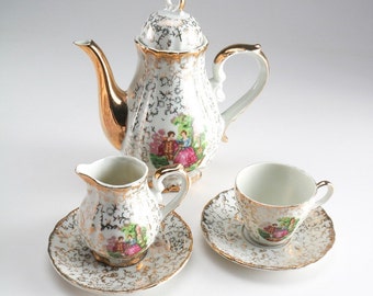 Haruta Empress bone china set featuring a couple in the garden, teapot with creamer, one teacup and two saucers with gold tone accents.
