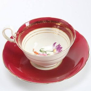 Può includere: Servizio da tè vintage. La tazza e il piattino sono rosso scuro con finiture dorate. L'interno della tazza è bianco con un motivo floreale. Il manico è bianco. Un classico servizio da tè.
