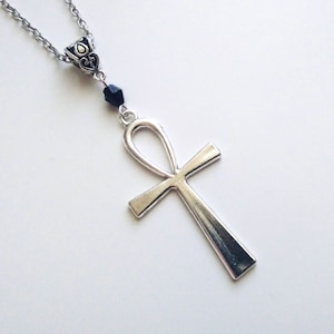 Könnte beinhalten: Eine silberne Ankh-Kette mit einer schwarzen Perle. Das Ankh ist ein Symbol des ewigen Lebens in der alten ägyptischen Mythologie.