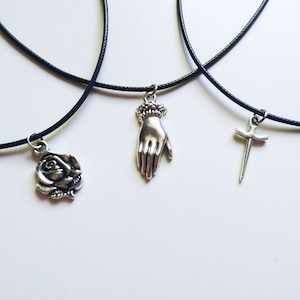 Könnte beinhalten: Drei zarte silberne Halsketten mit schwarzen Schnüren. Eine Halskette hat einen Rosenanhänger, eine andere einen Handanhänger und die dritte einen Schwertanhänger.