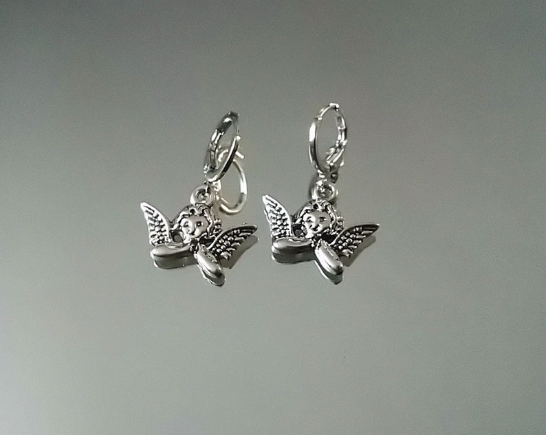 May include: Silver hoop earrings with a small angel charm hanging from each hoop.