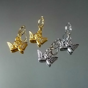 May include: Three pairs of angel charm earrings. Two pairs are silver and one pair is gold.